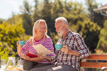Senior couple drinking coffee and reading in the backyard