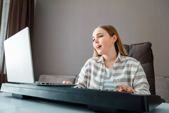 Woman learns music singing vocals playing piano online using laptop at home interior. Teenager girl sings song and plays piano synthesizer during video call, online lesson with teacher.