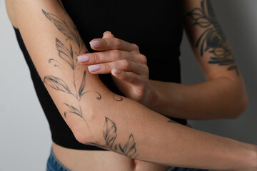 Woman applying cream on her arm with tattoos against light background, closeup - obrazy, fototapety, plakaty