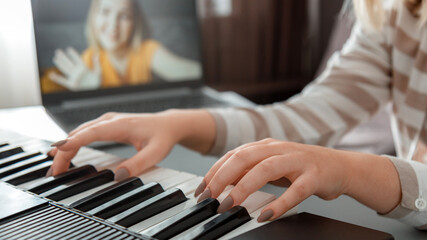 Obraz premium Woman playing piano during video call via laptop. Female hands musician pianist improves skills playing piano online classes with teacher. Online Music education. Long web banner