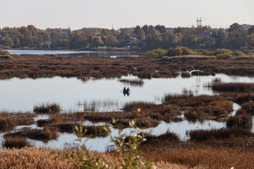 Landscape view of autumn colored river with small boat and fisherman fishing in the middle of river.