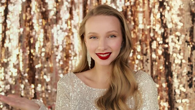 Fashion luxury portrait of woman sending blowing air kiss to the camera. Emotionally looking and smiling with red lips makeup, sparkling jewelry earrings on festive glittering background.