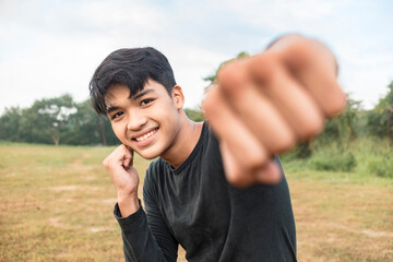A smiling young man in a dark gray sweatshirt doing shadow boxing outside a field. Throwing a right...