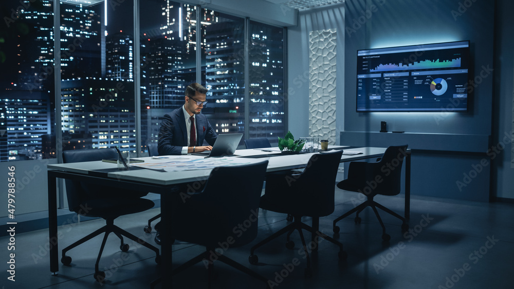Poster successful handsome businessman working on laptop computer in big city office late in the evening. f