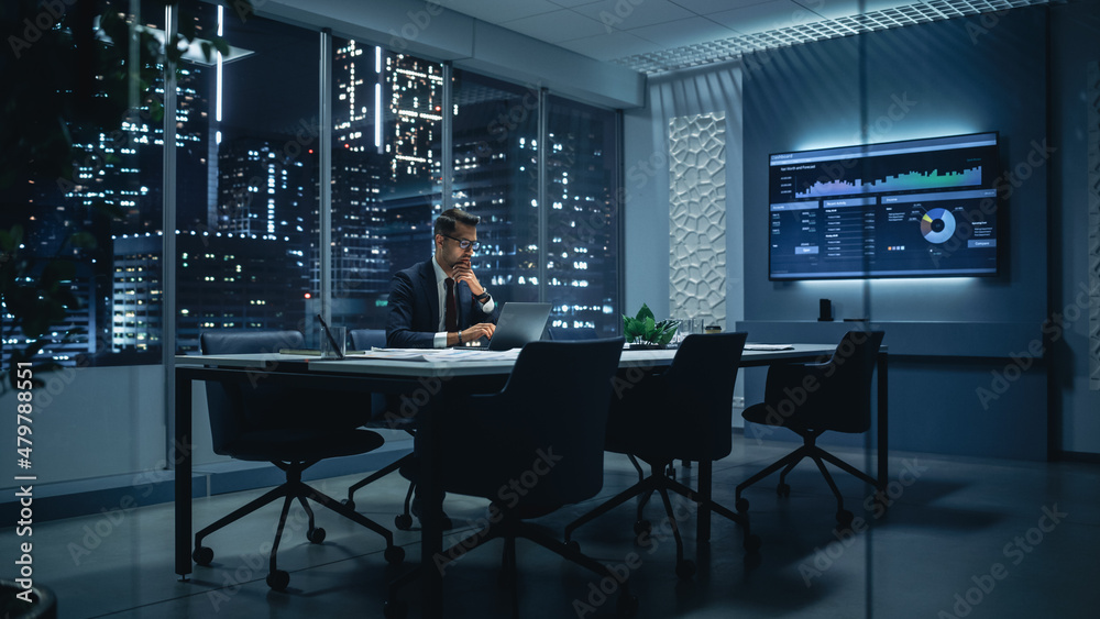 Poster successful handsome businessman working on laptop computer in big city office late in the evening. f
