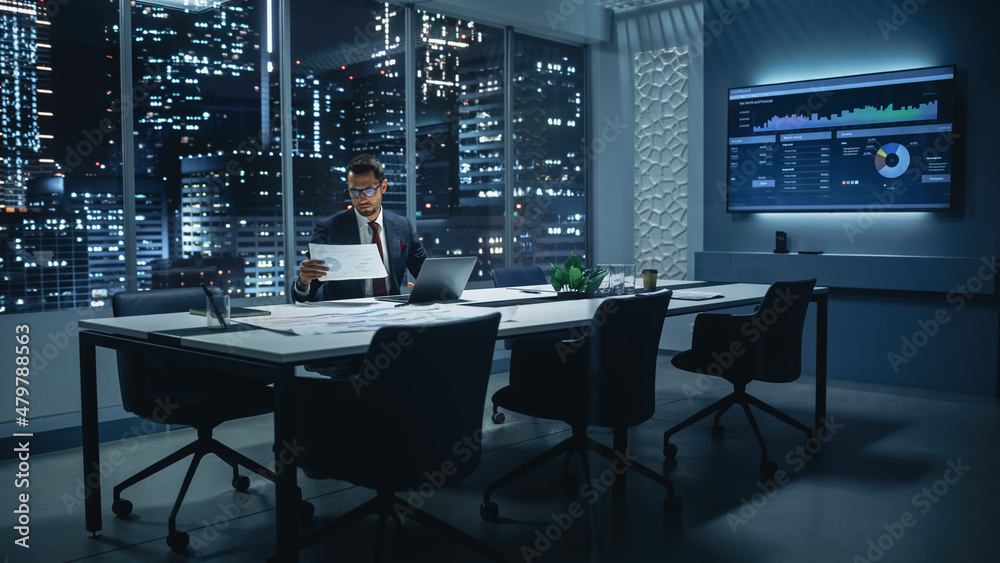 Poster successful handsome businessman working on laptop computer in big city office late in the evening. f