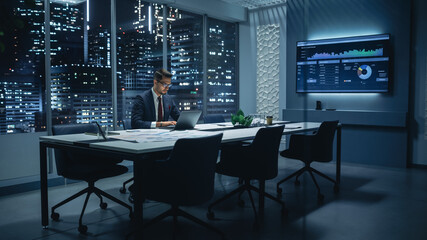 Successful Handsome Businessman Working on Laptop Computer in Big City Office Late in the Evening....