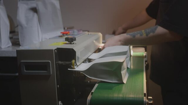 Packaging of roasted brown coffee in a zip pack. Conveyor belt for industrial coffee production. Filling machine. A man packs coffee in a bag