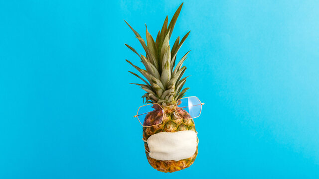 Pineapple funny face in sunglasses medical mask on color blue summer background. Travel concept pineapple in protective mask in coronavirus lockdown. Long web banner