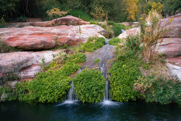 Fototapeta na wymiar double little waterfall surrounded by red rocks in summer at Sant Miquel del Fai, still water 
