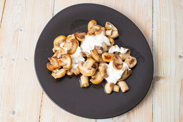 Fried champignon mushrooms with sour cream and garlic, on a black irregular plate, top view