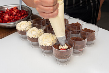 Pastry chef preparing step by step delicious dessert black forest or chip with chocolate biscuit, cream and fresh strawberries in shot glasses