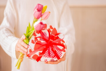 Valentine's Day card. arms holding gift box with heart shaped bowand flowes, Selective focus. Hand give gift with flowers. Congratulations, presentin,delivery