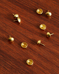 Golden thumbtacks on a wooden surface. Close-up product photo. 