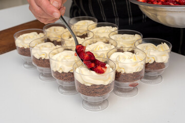 Pastry chef preparing step by step delicious dessert black forest or chip with chocolate biscuit, cream and fresh strawberries in shot glasses