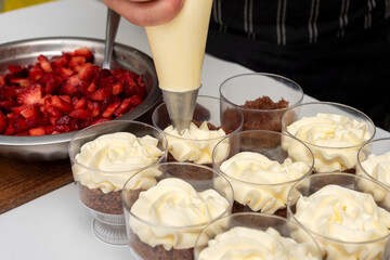 Pastry chef preparing step by step delicious dessert black forest or chip with chocolate biscuit, cream and fresh strawberries in shot glasses