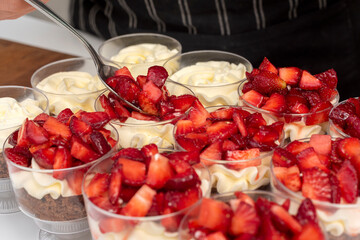 Pastry chef preparing step by step delicious dessert black forest or chip with chocolate biscuit, cream and fresh strawberries in shot glasses