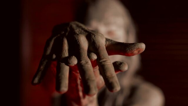 mysterious woman covered by mud is stretching palms to camera, enjoying mud wrap in spa