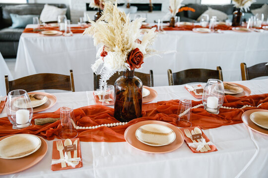 Terracotta-color runner on the table Candles and flowers decoration for a festive event party or wedding reception Candles in glass holders on white tablecloth wooden table Cropped photo