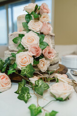 Close up of delicious three-tier white wedding cake covered with fresh pink and white roses at a wooden stand on the table Wedding Cake with whipped cream 