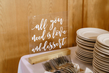 Glass sign that reads all you need is love and dessert on the table Wedding reception Plates and forks Acrylic wedding sign Dessert table sign Close up