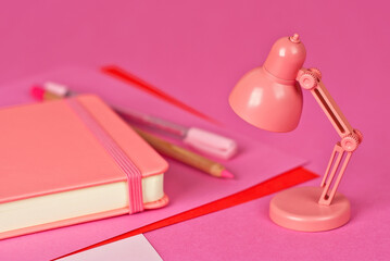 Fototapeta na wymiar Notepad on a pink background. Toy table lamp near the notebook. Copy space and free space for text near the lamp. The concept of roochy space and creative ideas.