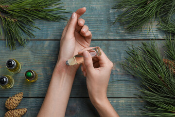 Woman applying pine essential oil on wrist at light blue wooden table, top view