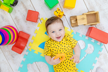 smiling happy baby boy plays in the nursery in a yellow bodysuit with bright colorful toys