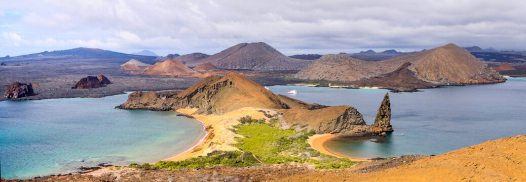 A panoramic view of Pinnacle Rock and the desolate landscape of Bartolomé Island in the Galapagos revealing the extensive volcanic activity and its limited vegitation.