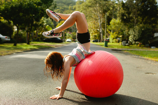 Young girl doing a handstand on an exercise ball on the road
