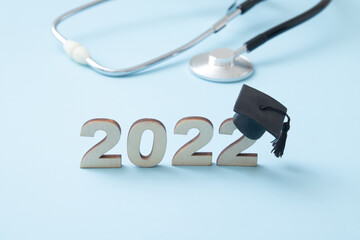 Number 2022 wearing a graduate cap with medical stethoscope on a blue background. Medical education...