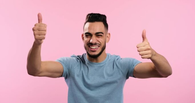 Excited man giving thumbs up gesture with both hands over pink background