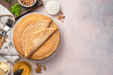 Traditional Russian blini on a light background with sour cream, honey and nuts.