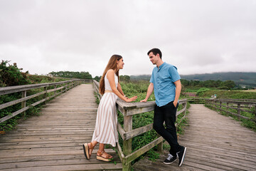Affectionate meeting of smiling couple who seem to flirt on a wooden walkway to the sea, romantic and positive emotion.