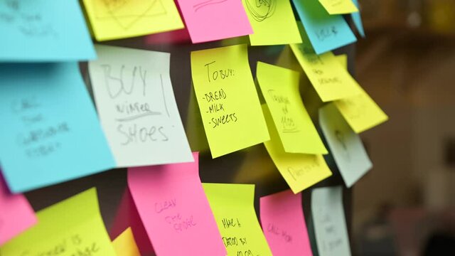 A woman puts a sticker with a to-do list and a shopping list on the refrigerator. A reminder of buy sweets, bread and milk