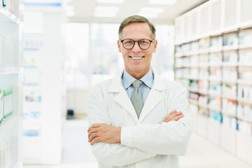 Naklejka na ściany i meble Smiling male caucasian middle-aged mature confident pharmacist druggist in white medical coat standing with arms crossed in pharmacy drugstore
