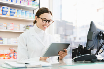 Chemist druggist pharmacist using digital tablet for checking looking for active substance, side effects of drugs remedy pills medicines online standing at cash point desk in pharmacy drugstore - Powered by Adobe