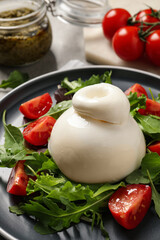 Delicious burrata salad with tomatoes and arugula on table, closeup