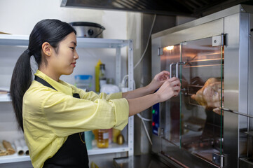 Young asian woman working in the kitchen and regulating ovens temperature