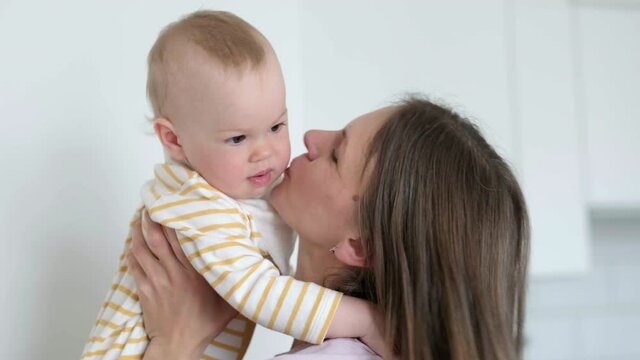 Little infant child laughing having fun and looking in camera. Happy Cheerful Family. Mother And Baby Kissing