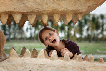 Little Girl inside of  dinosaur's mouth in dino park. Children play in Dinosaur Park.