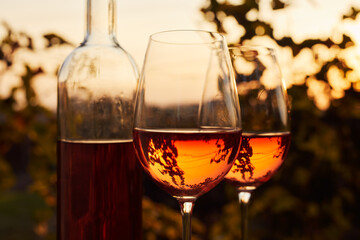 Two glasses full of rosé wine with a bottle outside at dusk