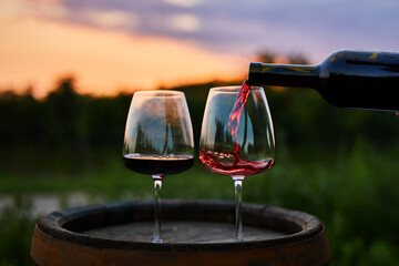 Pouring red wine from a bottle into a glass at dusk - 479808155