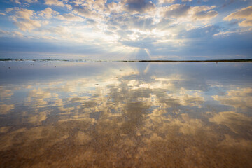 Ground level view of reflections of a dramatic sunset sky on a wet sandy beach