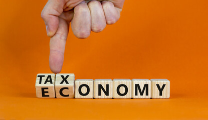 Taxonomy or economy symbol. Businessman turns cubes, changes the word economy to taxonomy. Beautiful orange table, orange background, copy space. Business, ecology and taxonomy or economy concept.