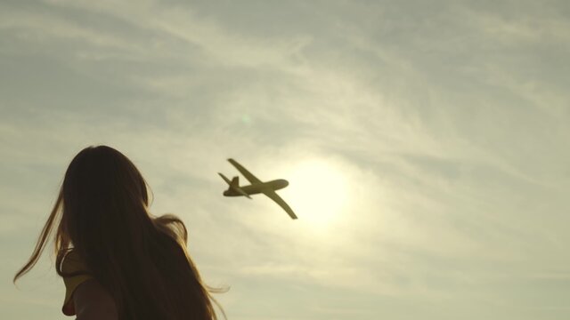 child plays a plane at sunset, girl launches flying toy plane into sky, childhood dream becoming pilot, adolescent childhood fantasy, future of free field path, fun kid journey, enjoy sunshine ahead