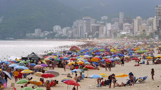 Establishing shot of busy Ipanema Beach showing people and colourful sun umbrellas during summer in Rio de Janeiro, Brazil.