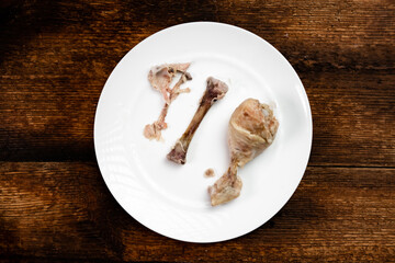 Two boiled half-eaten chicken legs on a white plate. Dark wooden background. Diet food.