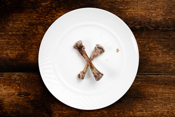 Chicken bones on a white plate. Dark wooden background. End of the meal.