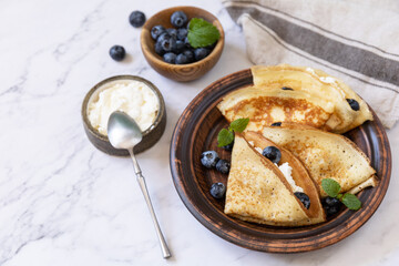 Celebrating Pancake day, healthy breakfast. Delicious homemade crepes with blueberries and ricota on a stone tabletop. Copy space.